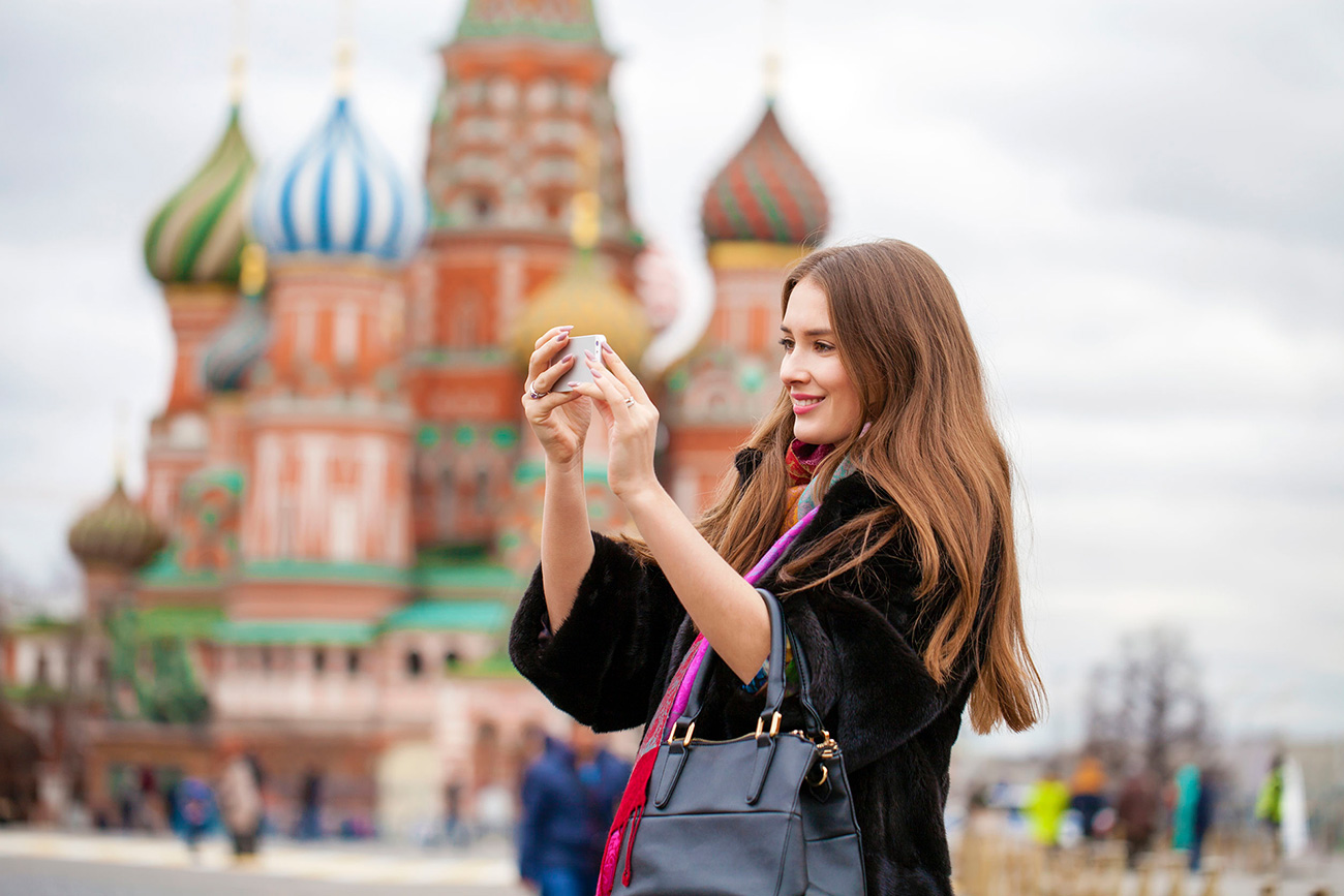 Young woman takes pictures on mobile phone on the background Red Square, Moscow Kremlin, Russia.
