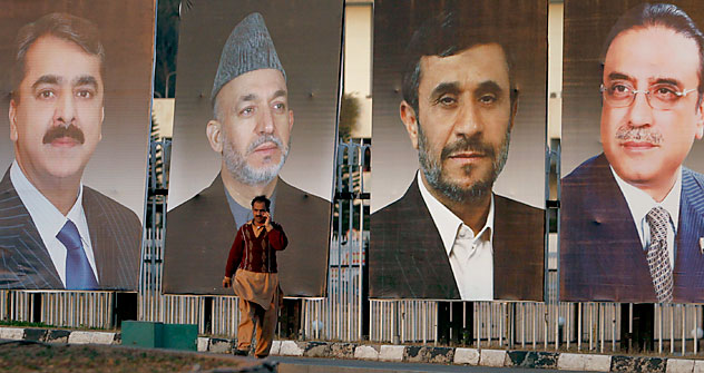 A man talks on his mobile phone as he walks past giant portraits of Afghanistan's President Karzai, Iran's President Ahmadinejad and Pakistan's President Zardari, along a road in Islamabad