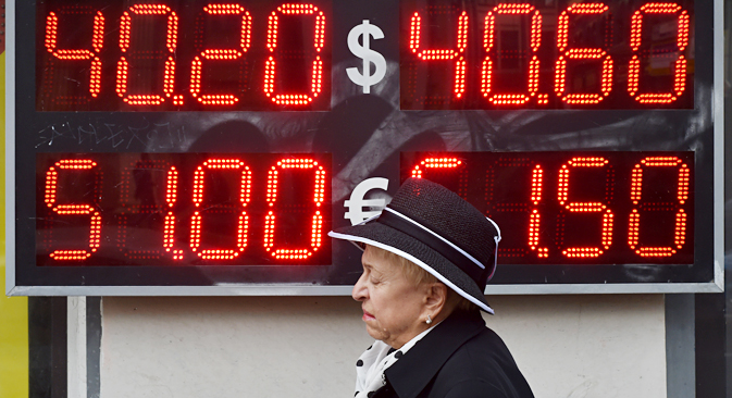 A woman walks under a board listing foreign currency rates against the Russian ruble, outside an exchange office in central Moscow, on October 13, 2014. Source: AFP/East News