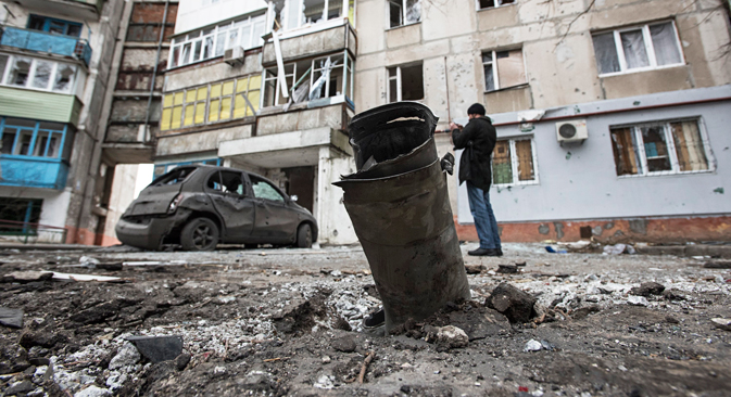 A piece of an exploded Grad missile is photographed as a man takes a photo of a burned car in the background, outside an apartment building in Vostochniy, district of Mariupol. Source: AP