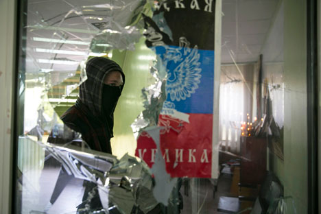 Un hombre enmascarado pasa por una ventana rota en el ayuntamiento de Mariupol en el este de Ucrania. Fuente: Reuters
