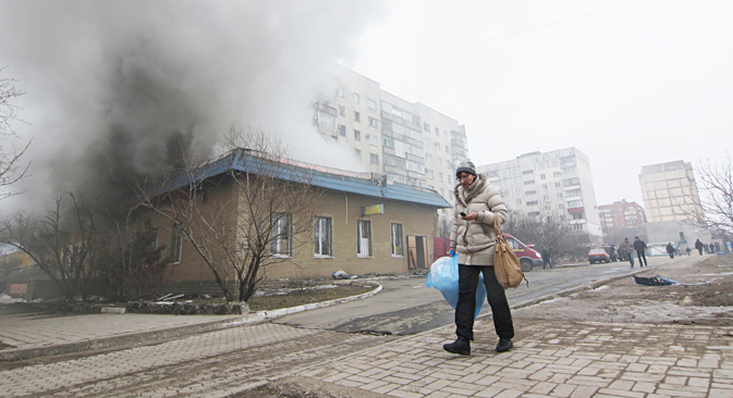 Residente de Mariúpol pasa junto a una casa en llamas durante el ataque producido el pasado sábado, 24 de enero. Fuente: AP