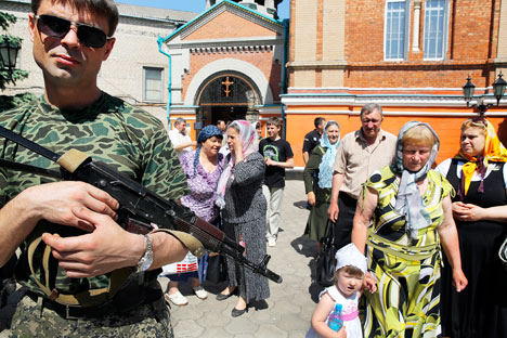 Un rebelle armé se tient près de croyants orthodoxes locaux sortant de la cathédrale Alexandre Nevski, après une messe dominicale dans la ville ukrainienne de Slaviansk, le 18 mai 2014. Crédit : Reuters