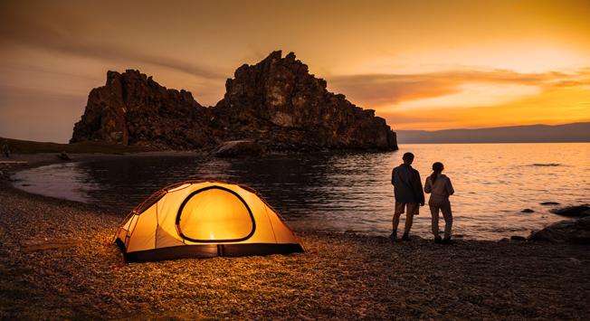 Couple stand at tent and Baikal lake shore and looking at the sunset. Source: Shutterstock / Legion-Media
