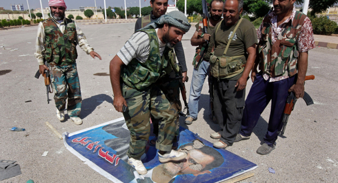 A Free Syrian Army fighter from the Al-Faruk brigade, center, steps on a portrait of Syrian President Bashar Assad