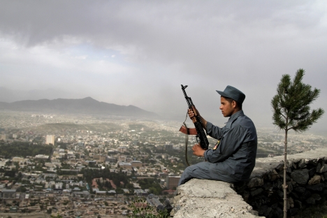Un poliziotto afghano siede di guardia su un muro che domina Kabul (Foto: AP)